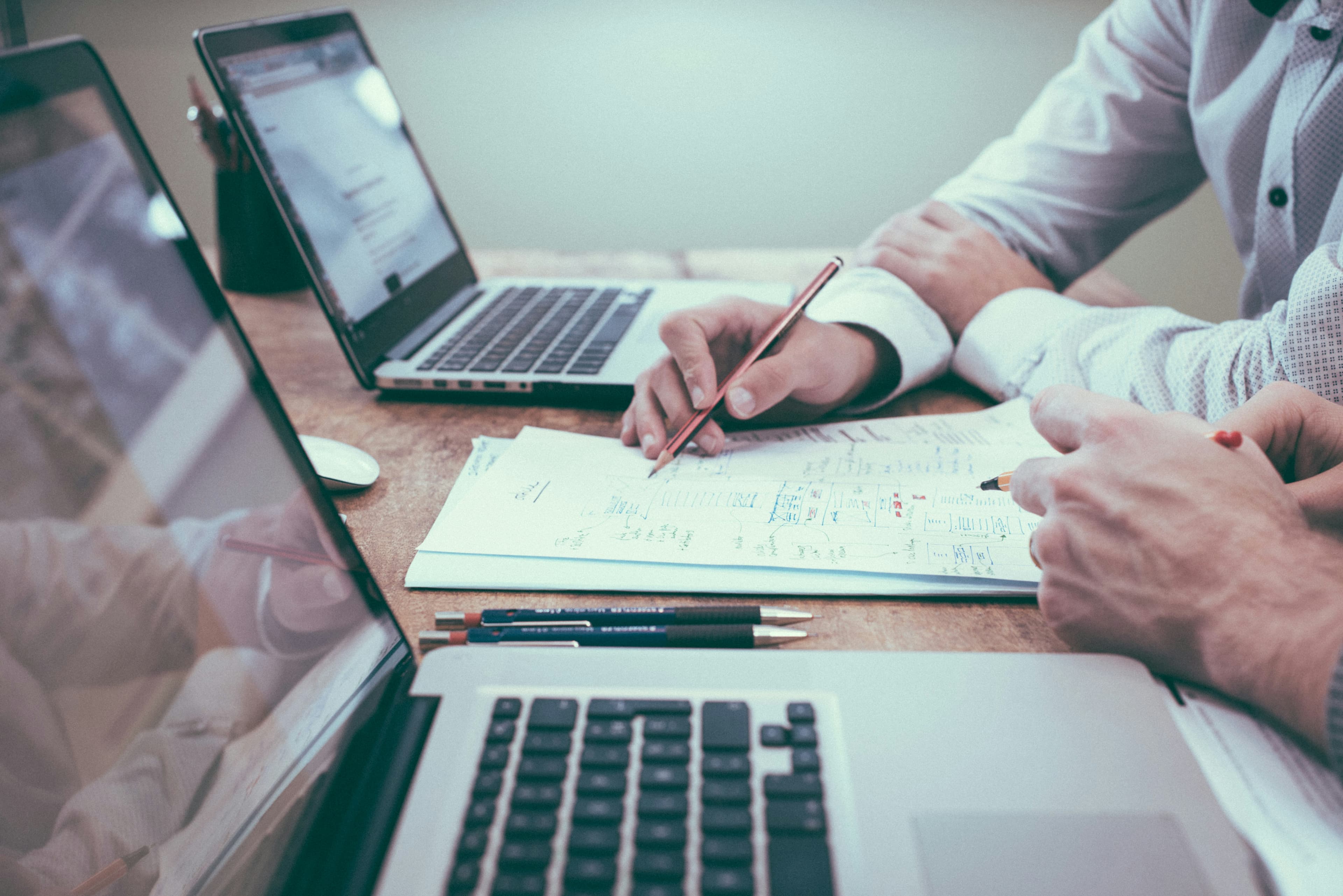 Duas pessoas sentadas à mesa conferindo papéis e anotações ao lado de notebooks.